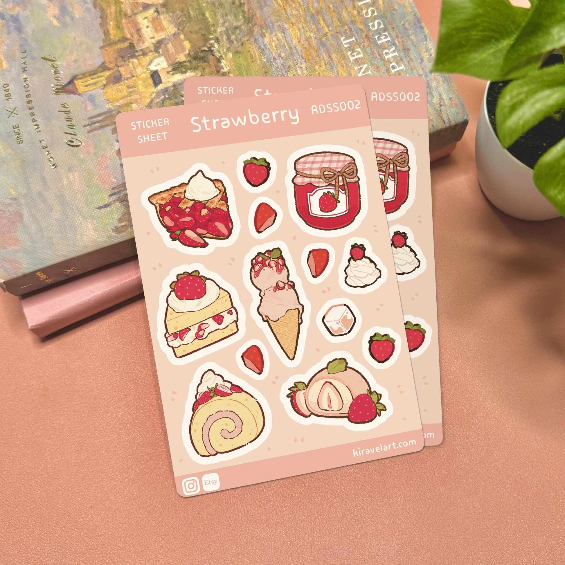 Sheet of strawberry-themed stickers on a pink surface with a plant and book in the background.